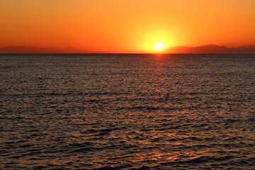 Calm dark morning sea and rising orange sun. Dawn by the sea, landscape travel photography. Distant hills over the sea and colorful sunrise.