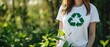 Woman in white t-shirt with green recycling symbol standing in lush garden. Close-up