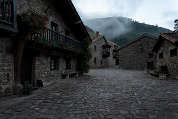 Wall Mural - A quiet, empty courtyard with a few houses in the background. Fog falling over the houses in a dark and calm atmosphere. Barcena Mayor, Saja-Besaya Natural Park, Cantabria, Spain.