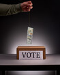 Hand holding hundred dollar bill on hook over voting box
