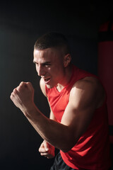 Young excited man in red sportswear keeping clenched fist in front of his face during kick training without boxing gloves