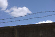A concrete wall with barbed wire on top against a blue sky background