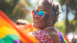 © Prasanth - Happy black senior gay lesbian woman celebrating pride festival parade with a rainbow flag on a sunny summer day. Candid gay pride celebrations with inclusive and diverse homosexual mature people. AI