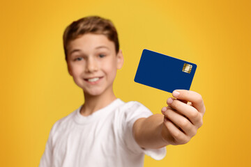 No cash money. Smiling boy showing credit card at camera, orange studio background