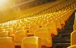 Rows of empty yellow stadium seats under sunlight.