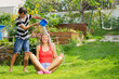 Boy playfully pour water from bucket onto seated woman in garden