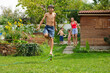 Teenager jump through water droplets from hose in green backyard