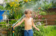 A cheerful child having fun with water hose in green backyard