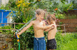 Happy young boy and girl enjoy refreshing water game with hose