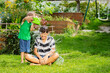 Kid sprinkle his seated brother with water from bucket in garden