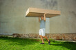 Male person outdoors carrying a big, flat box on top of his head