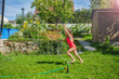 Girl in pink swimwear running through the spray of garden hose