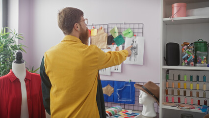 Poster - A bearded man in a yellow shirt points at a fashion sketch in a well-organized tailor shop with colorful thread spools.