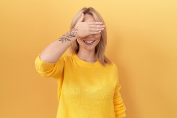 Wall Mural - Young caucasian woman wearing yellow sweater smiling and laughing with hand on face covering eyes for surprise. blind concept.