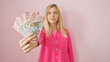 Young blonde woman in pink blouse holding new zealand currency against a plain background.