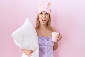 Poster - Young caucasian woman wearing pajama hugging pillow and drinking coffee angry and mad screaming frustrated and furious, shouting with anger looking up.