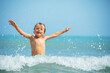 A joyful young boy with arms wide open, playing in the sea waves