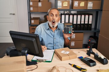 Poster - Amazed senior man with open mouth showing a face of disbelief in an office, scared as he holds calculator in surprise