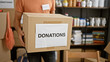 © Krakenimages.com - Hispanic man carrying donation box in a cluttered volunteer warehouse filled with shelves and supplies.