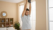 © Krakenimages.com - A handsome young man with a beard exercises lifting a dumbbell in a well-lit, cozy bedroom interior.