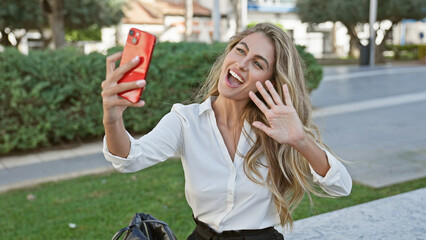 Canvas Print - Joyous young blonde woman confidently smiling while enjoying a casual phone call in the park's sunlight. lifestyle portrait showcases her natural beauty, confidently talking on mobile device.