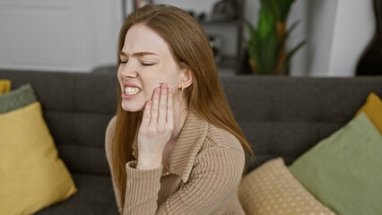 Sticker - A young woman expressing pain while touching her cheek in a cozy living room setting.