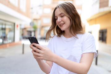 Wall Mural - Young caucasian woman smiling confident using smartphone at street