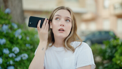 Poster - Young caucasian woman listening audio message by the smartphone with serious expression at park