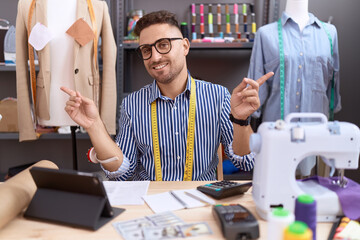 Poster - Hispanic man with beard dressmaker designer working at atelier smiling confident pointing with fingers to different directions. copy space for advertisement