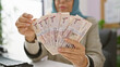 © Krakenimages.com - Middle-aged woman counting saudi riyal banknotes at her office desk, indicating finance and business in a workplace setting.