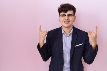 Canvas Print - Young non binary man with beard wearing suit and tie shouting with crazy expression doing rock symbol with hands up. music star. heavy concept.