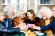 Happy group of senior people laughing and enjoying coffee at cafeteria bar. Retired generation community having fun gathered on terrace toasting hot drink. Elderly friendship lifestyle concept.