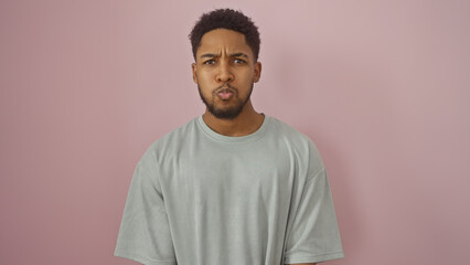 Portrait of a young adult african american man in casual clothing standing against a pink isolated background, exuding confidence and style.