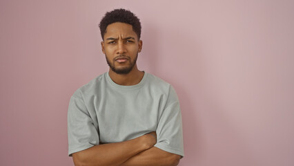 Handsome adult black man with arms crossed standing against an isolated pink wall, portraying confidence.