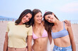 © CarlosBarquero - Three young Caucasian friends posing happy on beach vacation portrait. Group of beautiful women hugging standing looking smiling at camera on sunny summer trip. Generation z female people in swimwear