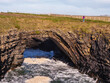Tourist enjoy stunning Bridges of Ross in county Clare, Ireland. Rock formation arched over ocean creating natural bridge. Popular tourist landmark and point of interest. Warm sunny day.