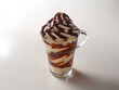 Coupe de glace de type dame blanche ou sunday avec des boules de glace vanille surmontées de sauce chocolat et de crème fouettée, fond blanc