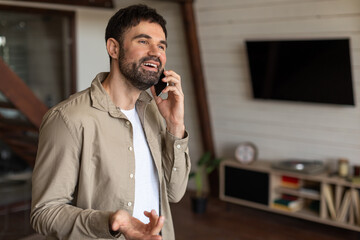Poster - A man is engaged in a phone call while standing in a modern living room, holding a cell phone to his ear. The room is tastefully decorated with a sofa, coffee table, and plants, copy space