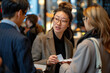 Asian woman in a stylish gray blazer and round glasses engages in a lively conversation with colleagues at a networking event. 