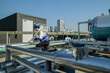 © ultramansk - A young engineer checks equipment on a rooftop amidst urban skyline, clipboard in hand, ensuring system functionality.Engineer in safety vest and helmet conducting maintenance on rooftop machinery.