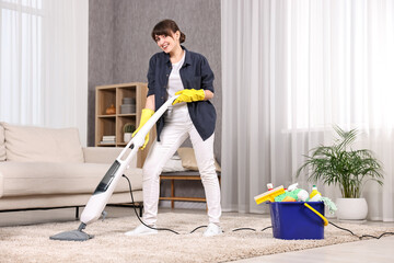 Wall Mural - Happy young housewife vacuuming carpet at home