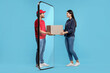 © New Africa - Courier delivering parcel to woman through huge smartphone on light blue background