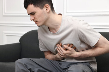 Wall Mural - Young man suffering from heart hurt on sofa at home