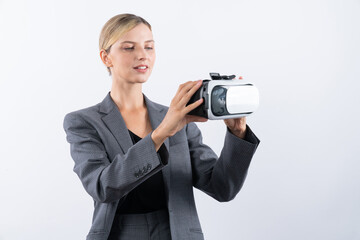 Wall Mural - Caucasian business woman holding VR glass while standing at white background. Professional project manager looking visual reality goggle while wearing suit. Innovation technology concept. Contraption.