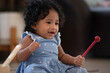 African baby girl with curly hair holding children's xylophone stick, smile happy at someone on floor