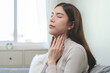 Sickness in inflaming asian young woman, girl use hand check self touch at sore throat, pain thyroid gland on neck or disease reflux, acid of suffer people on wall background. Medical and healthcare.