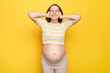 Irritated brown haired pregnant woman with bare belly posing isolated over yellow background covering her eyes with palm hearing loud noise unpleasant sounds