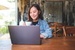 Portrait image of a young woman drinking coffee while working on laptop computer in cafe