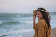 Portrait image of a beautiful woman holding hat while strolling on the beach