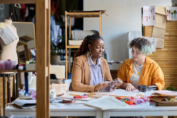 Portrait of Black young woman as social worker helping girl with disability sewing clothes in vocational training class copy space